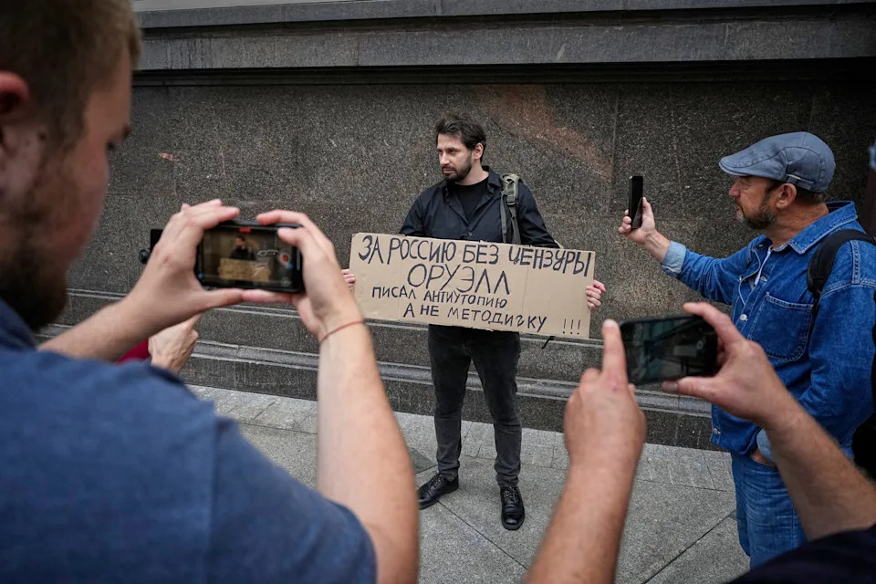 Hombre sosteniendo un cartel en ruso mientras otros toman fotos con sus teléfonos