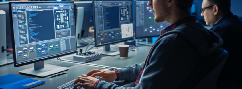 Dos personas trabajando en computadoras con código en pantalla