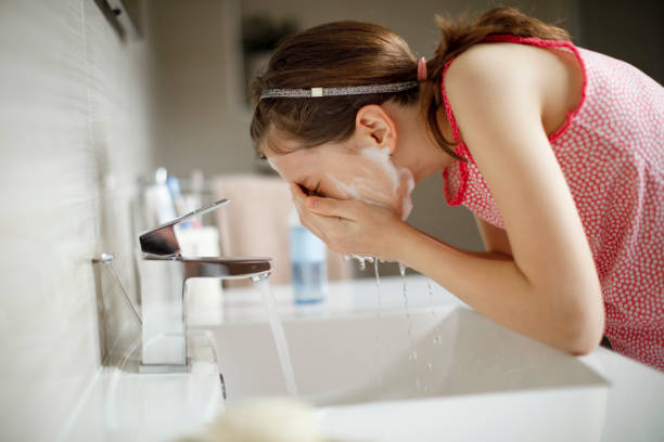 Girl washing face at sink with water flowing
