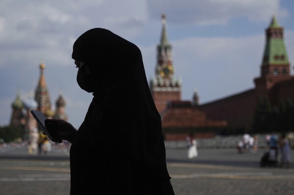 Mujer con mascarilla usando su teléfono frente al Kremlin