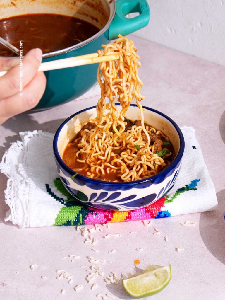 Close-up of birria ramen being assembled, with a side of red consommé