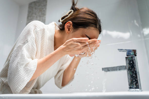Woman washing face at sink with water splashing