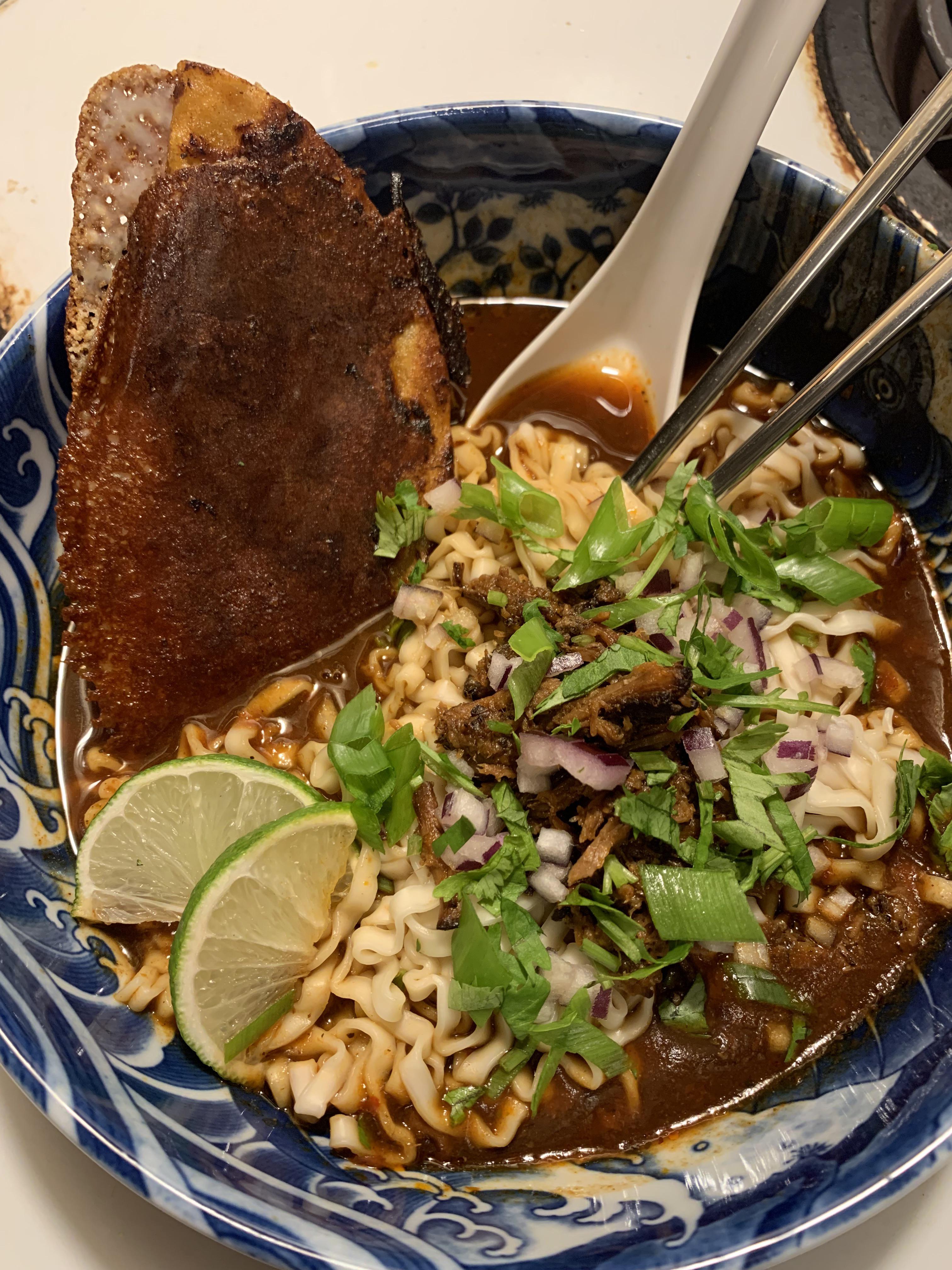 Overhead shot of birria ramen ingredients — dried chiles, beef, aromatics, noodles